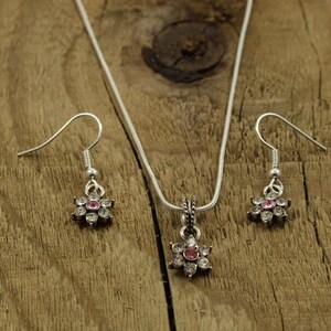 May include: A silver necklace and earrings set with a flower pendant and matching earrings. The flower pendant and earrings have clear and pink rhinestones.
