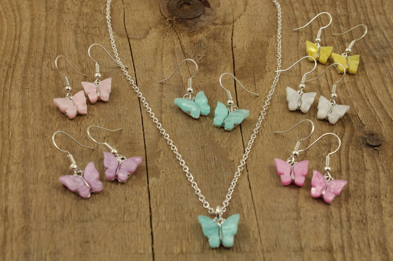 May include: A set of butterfly earrings and a necklace with a matching butterfly pendant. The earrings and pendant are available in a variety of colors, including pink, purple, blue, white, and yellow.