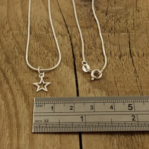 May include: A silver chain necklace with a star pendant. The necklace is 18 inches long and the star is about 1/2 inch wide. The necklace is shown on a wooden surface with a ruler for scale.