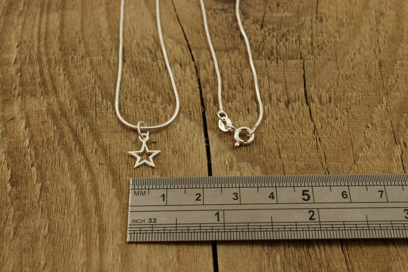 May include: A silver chain necklace with a star pendant. The necklace is 18 inches long and the star is about 1/2 inch wide. The necklace is shown on a wooden surface with a ruler for scale.