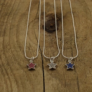 May include: Three silver chain necklaces with star-shaped pendants. The stars are covered in small, colorful rhinestones. The stars are red, gray, and blue.