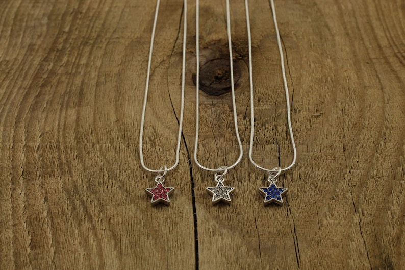 May include: Three silver chain necklaces with star-shaped pendants. The stars are covered in small, colorful rhinestones. The stars are red, gray, and blue.
