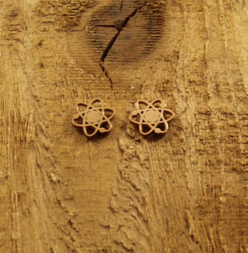 May include: A pair of gold-toned atom earrings on a wooden surface.