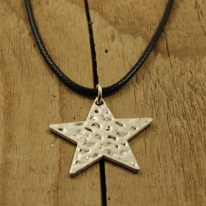 May include: A silver star pendant necklace with a hammered texture, hanging from a black leather cord.