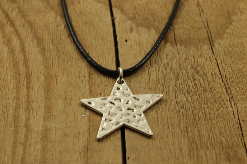 May include: A silver star pendant necklace with a hammered texture, hanging from a black leather cord.