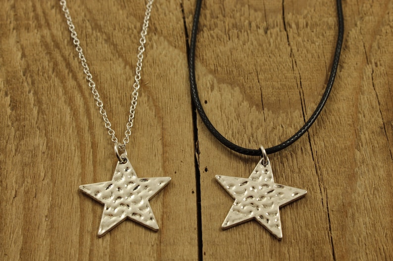May include: Two silver star necklaces, one on a silver chain and the other on a black cord. Both stars have a hammered texture.