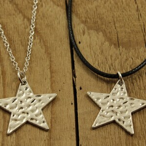 May include: Two silver star necklaces, one on a silver chain and the other on a black cord. Both stars have a hammered texture.