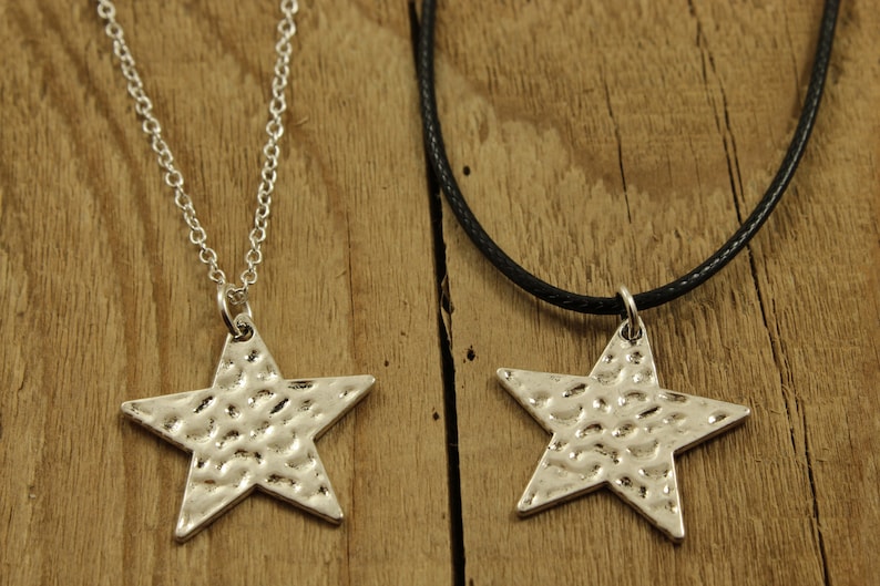 May include: Two silver star necklaces, one on a silver chain and the other on a black cord. Both stars have a hammered texture.