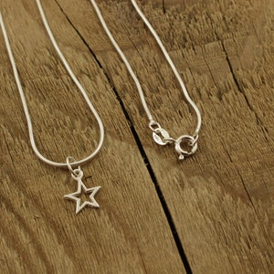 May include: A silver chain necklace with a star-shaped pendant. The necklace is on a wooden surface.