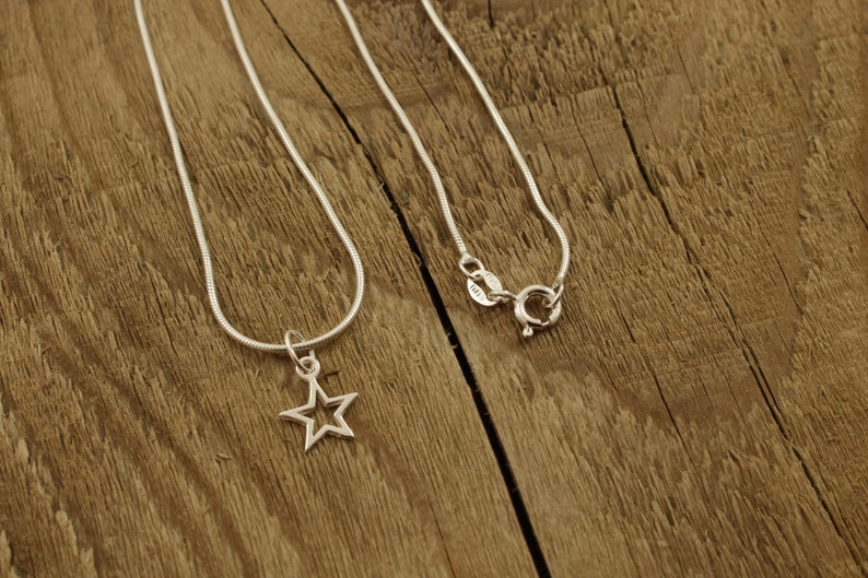 May include: A silver chain necklace with a star-shaped pendant. The necklace is on a wooden surface.