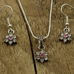 May include: A silver necklace and earrings set with a pink and clear crystal flower pendant and matching earrings.