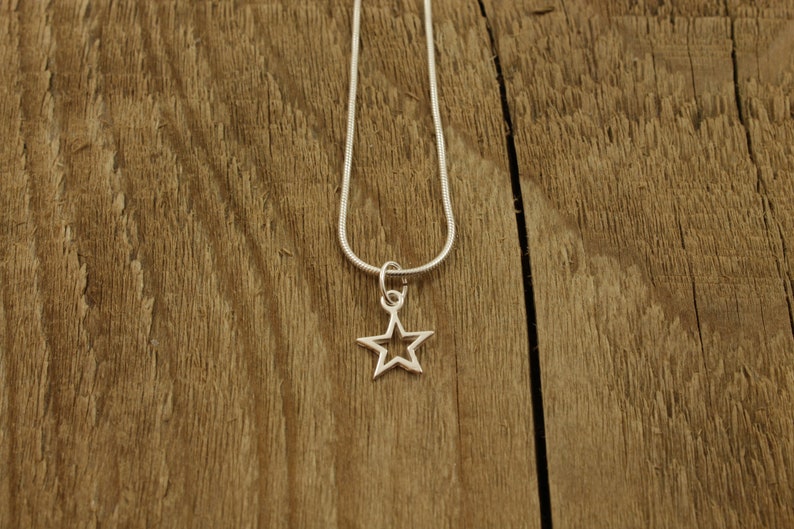 May include: A silver chain necklace with a small, open star pendant. The necklace is displayed on a wooden surface.