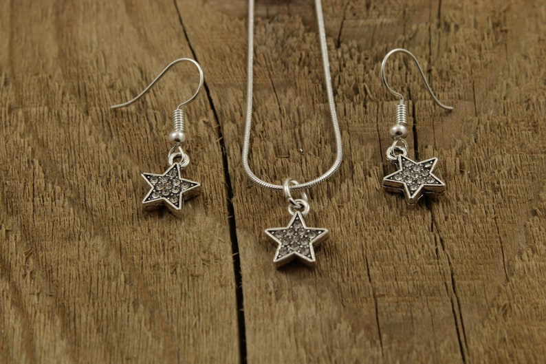 May include: A silver necklace and earrings set with star-shaped pendants encrusted with clear rhinestones.