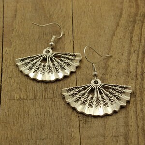May include: A pair of silver earrings with a fan-shaped design. The earrings are made of metal and have a delicate, intricate design.
