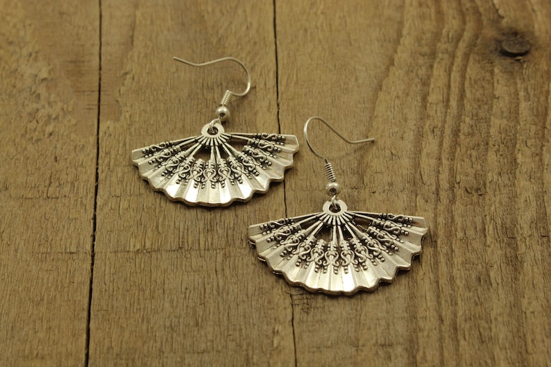 May include: A pair of silver earrings with a fan-shaped design. The earrings are made of metal and have a delicate, intricate design.