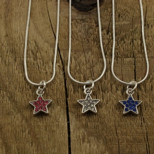May include: Three silver chain necklaces with star-shaped pendants. The stars are covered in rhinestones, one red, one clear, and one blue.
