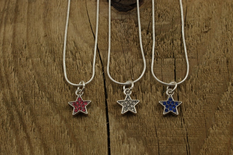 May include: Three silver chain necklaces with star-shaped pendants. The stars are covered in rhinestones, one red, one clear, and one blue.