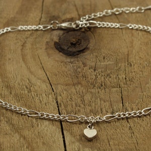 May include: A silver chain anklet with a small heart charm. The anklet is on a wooden surface.