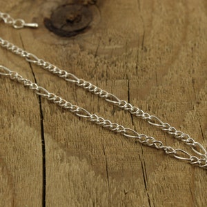 May include: A silver chain necklace with a small heart charm pendant. The chain is a figaro style with alternating links.