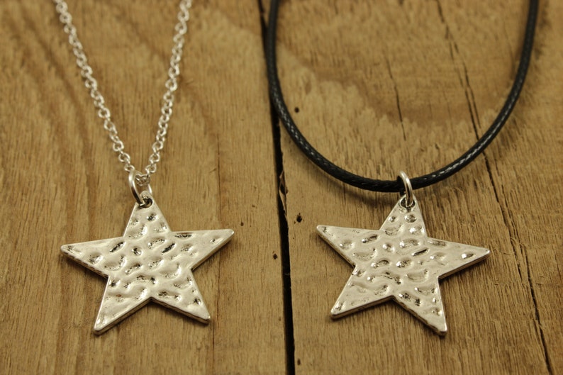 May include: Two silver star necklaces, one on a silver chain and the other on a black cord. Both stars have a hammered texture.