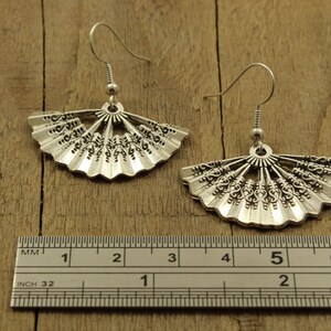 May include: Silver fan-shaped earrings with intricate details, measured against a ruler showing 5 centimetres in length.