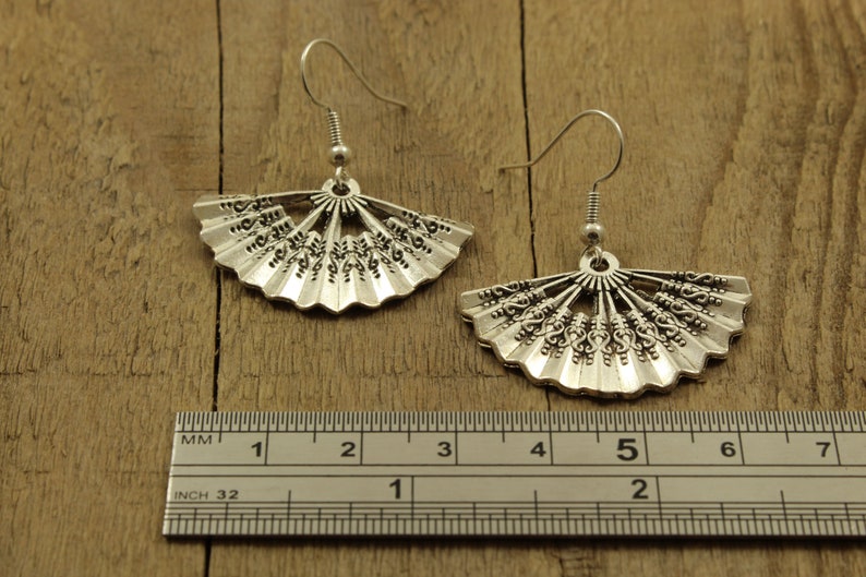 May include: Silver fan-shaped earrings with intricate details, measured against a ruler showing 5 centimetres in length.