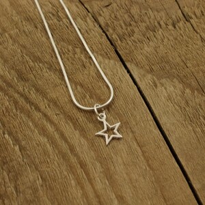 May include: A silver chain necklace with a star-shaped pendant. The star has an open center and is hanging on a silver chain.