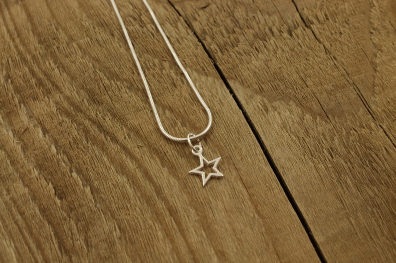 May include: A silver chain necklace with a star-shaped pendant. The star has an open center and is hanging on a silver chain.