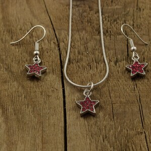 May include: A silver necklace and earrings set with a red star pendant and matching earrings. The star is made of rhinestones.