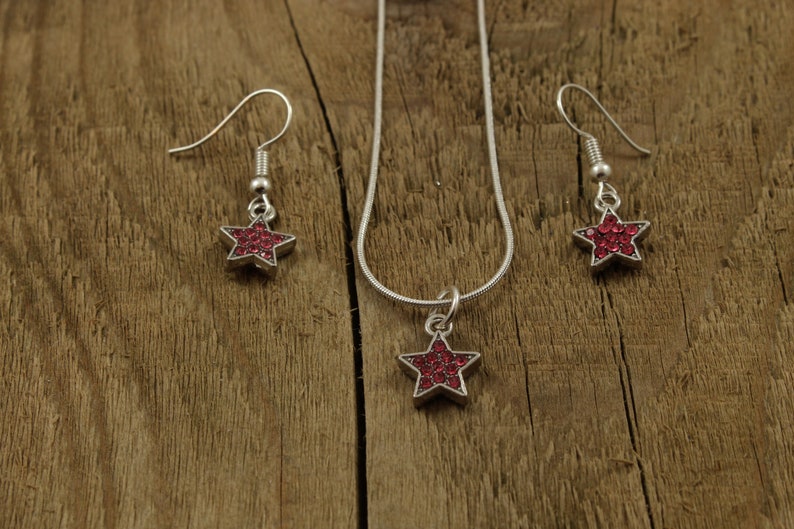 May include: A silver necklace and earrings set with a red star pendant and matching earrings. The star is made of rhinestones.