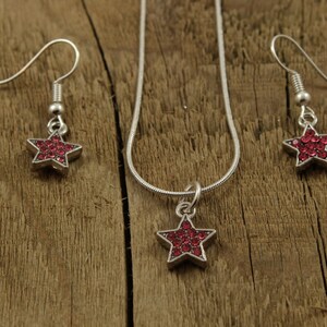 May include: A silver necklace and earrings set with a red star pendant and matching earrings. The star is made of small red rhinestones.