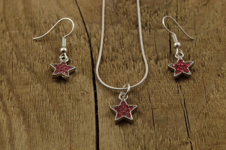 May include: A silver necklace and earrings set with a red star pendant and matching earrings. The star is made of small red rhinestones.