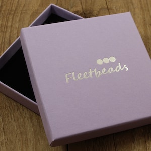 May include: A lavender colored box with a silver logo that says "Fleetbeads" with three silver circles above the text.