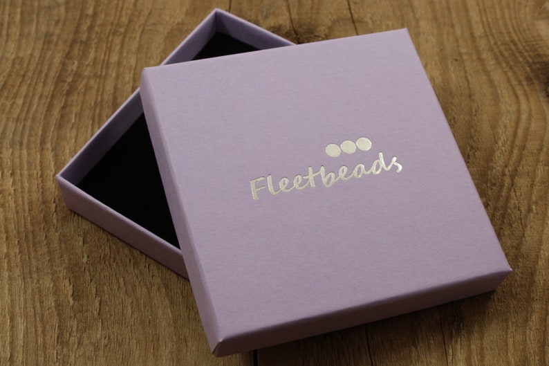 May include: A lavender colored box with a silver logo that says "Fleetbeads" with three silver circles above the text.