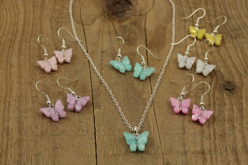 May include: A set of butterfly earrings and a necklace with a matching butterfly pendant. The earrings and pendant are made of iridescent pastel colors, including pink, purple, blue, yellow, and white.