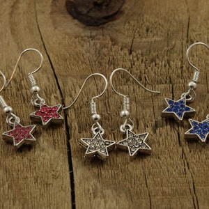 May include: Three pairs of silver star-shaped earrings with crystal accents. The stars are red, blue, and clear.