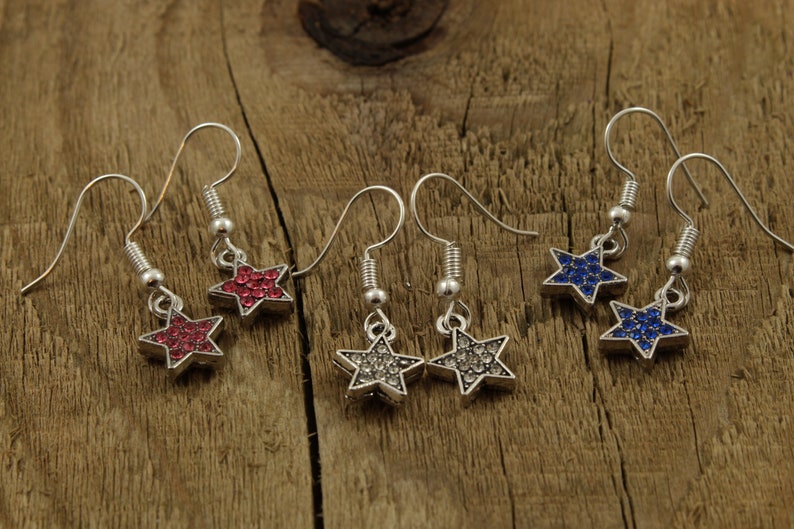 May include: Three pairs of silver star-shaped earrings with crystal accents. The stars are red, blue, and clear.