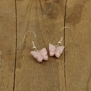 May include: A pair of silver butterfly earrings with pink butterfly charms. The earrings are hanging from a wooden surface.