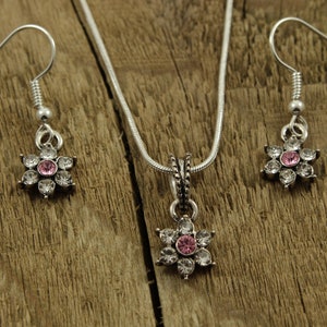 May include: A silver necklace and earrings set with a pink and white flower pendant and matching earrings.