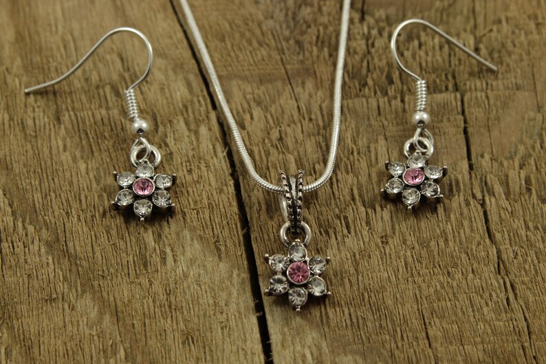 May include: A silver necklace and earrings set with a pink and white flower pendant and matching earrings.