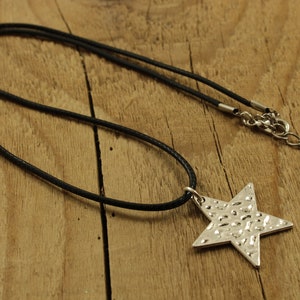 May include: A silver star pendant necklace with a textured surface, hanging on a black cord.