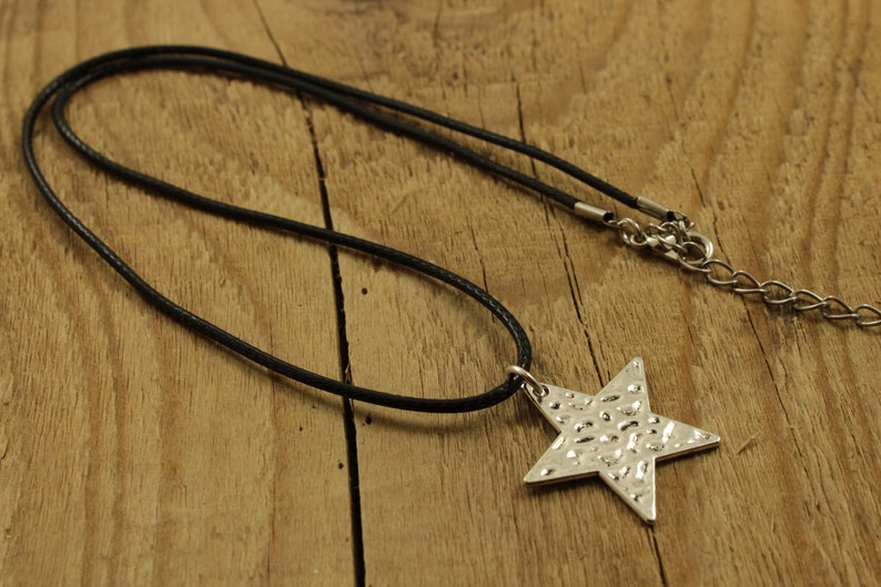 May include: A silver star pendant necklace with a textured surface, hanging on a black cord.