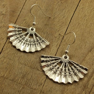 May include: A pair of silver earrings shaped like a fan with intricate details. The earrings have a hook fastening.