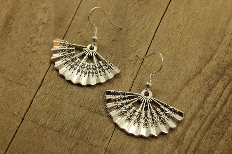 May include: A pair of silver earrings shaped like a fan with intricate details. The earrings have a hook fastening.