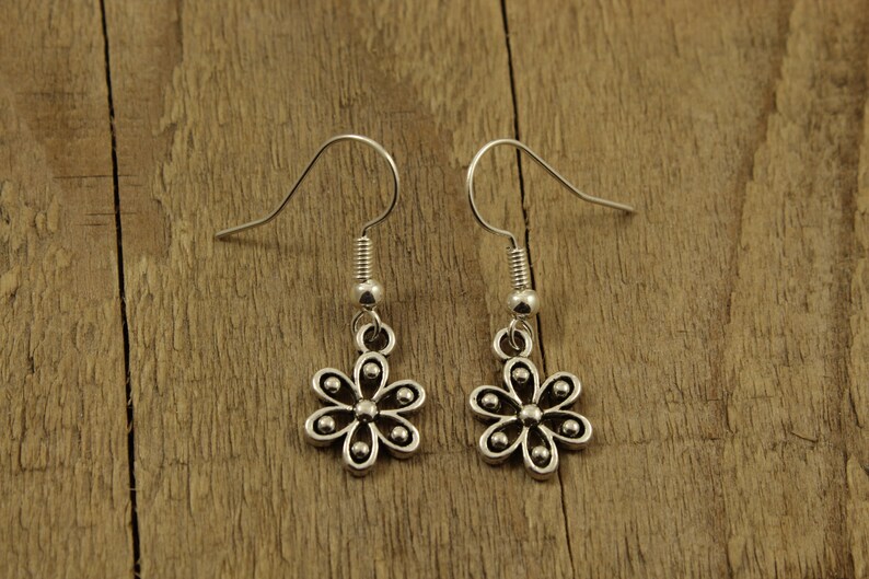 May include: A pair of silver-coloured flower earrings. Each earring has a small, six-petal flower charm with a small bead in the centre of each petal. The earrings have a simple hook design for pierced ears.
