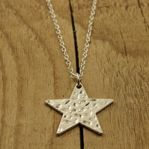 May include: A silver necklace with a hammered star pendant. The necklace is on a wooden surface.