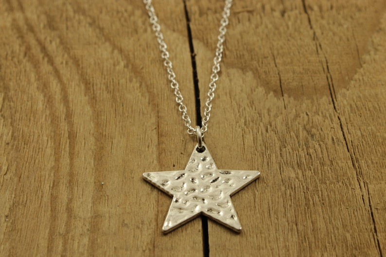 May include: A silver necklace with a hammered star pendant. The necklace is on a wooden surface.