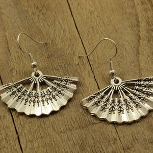 May include: A pair of silver earrings with a fan-shaped design. The earrings are made of metal and have a delicate, intricate pattern.