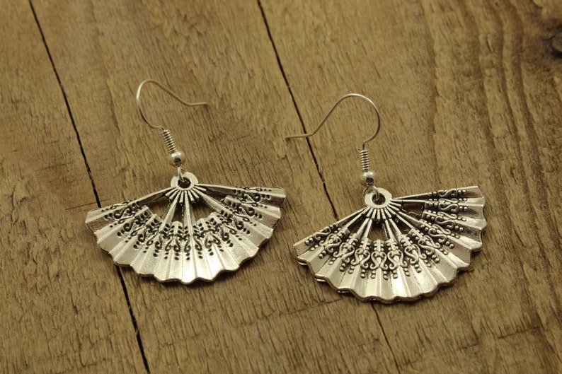 May include: A pair of silver earrings with a fan-shaped design. The earrings are made of metal and have a delicate, intricate pattern.