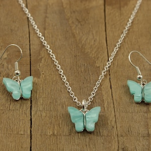 May include: A silver necklace and earrings set with a light blue butterfly pendant and matching earrings.